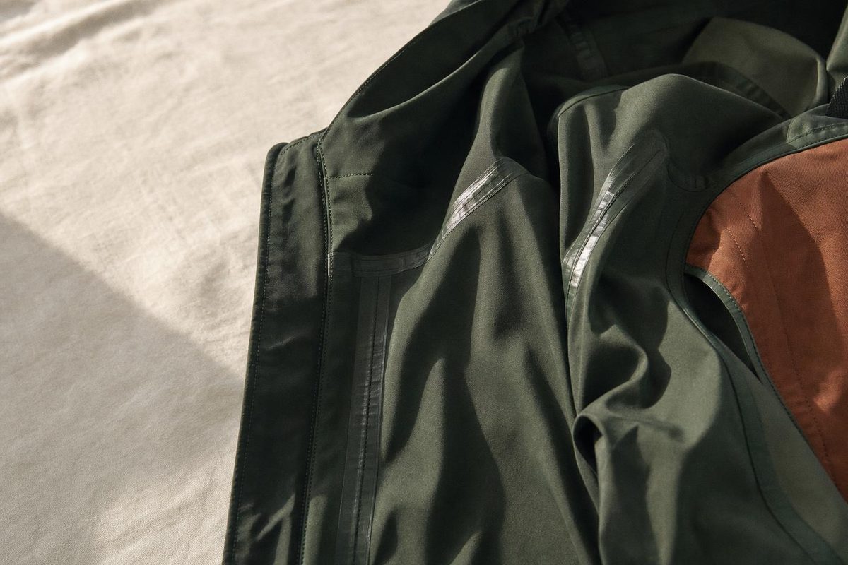 Interior de una chaqueta de softshell verde oscuro con la cinta termosellada cubriendo las costuras, sobre lino claro